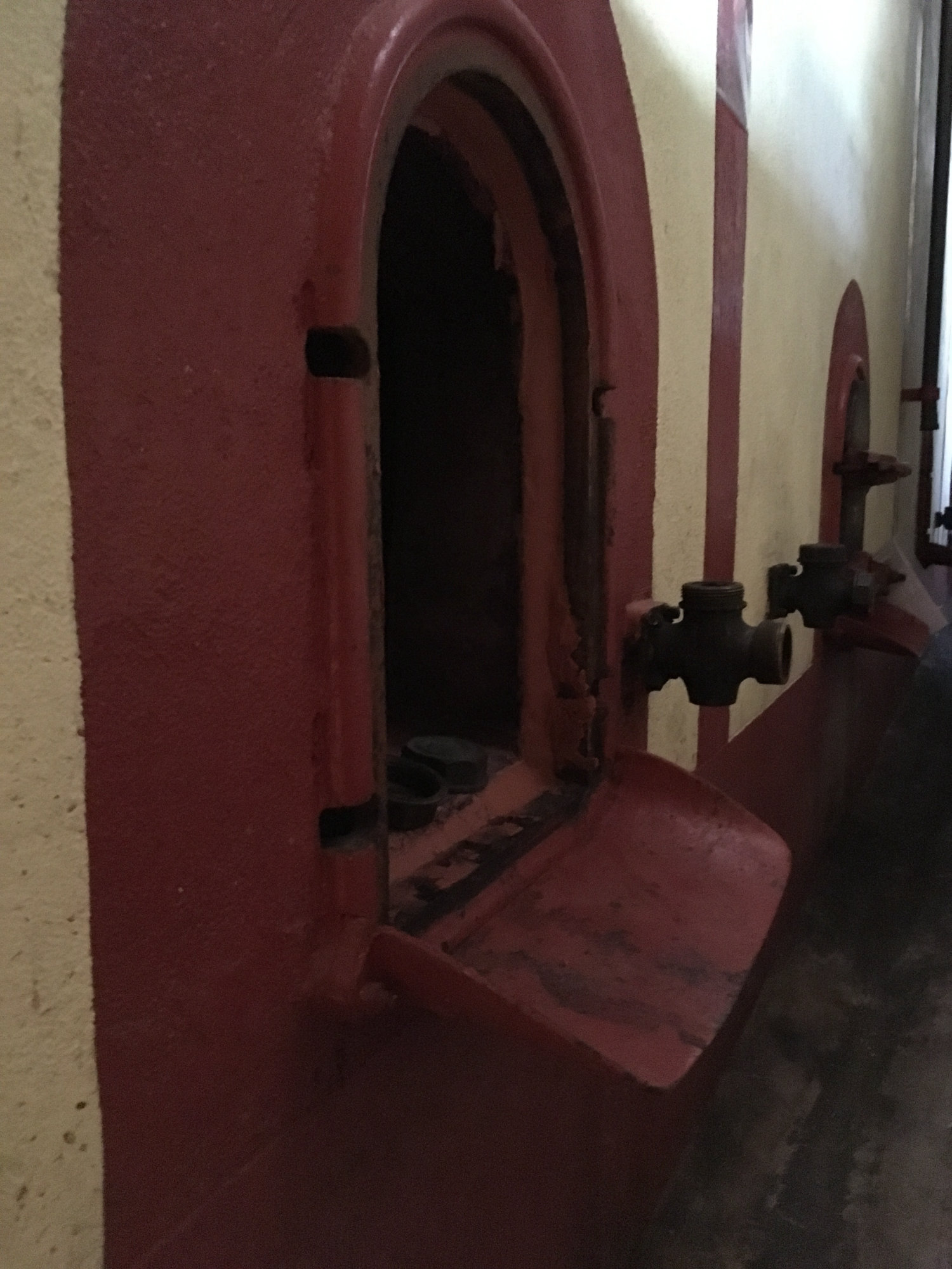 Red-painted concrete cuves with arched iron access doors and brass valves in the cellar at Domaine des Favards.